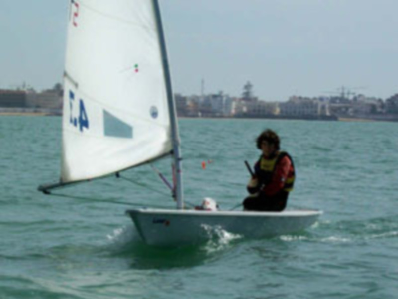 Un regatista disfruta de una jornada de vela en el mar, navegando en un velero ligero con el viento en favor.