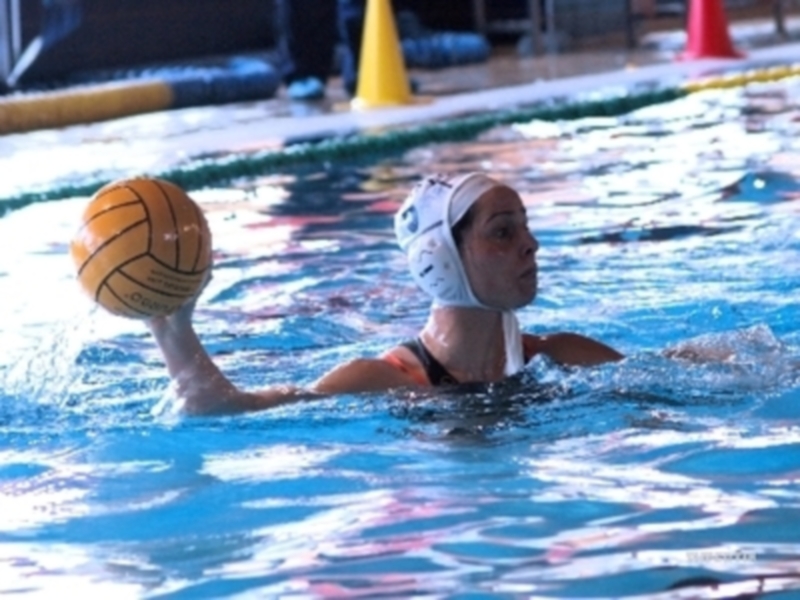 Jugadora de waterpolo en acción, sosteniendo el balón en un piscina cubierta.