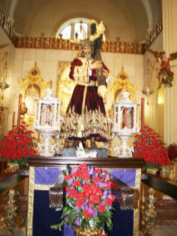 Imagen de una iglesia con una estatua religiosa en el centro, rodeada de flores y adornos.