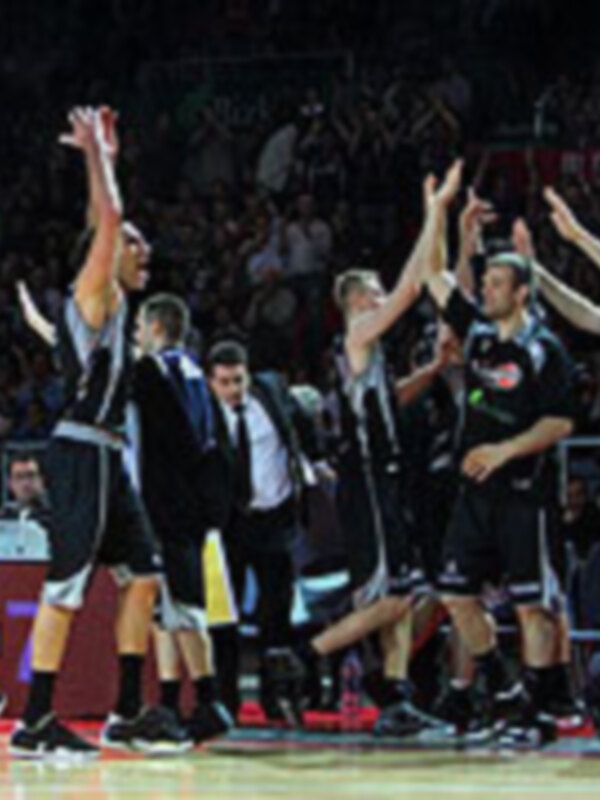 Un equipo de baloncesto celebrando una victoria en el estadio, con los jugadores levantando los brazos en el aire.