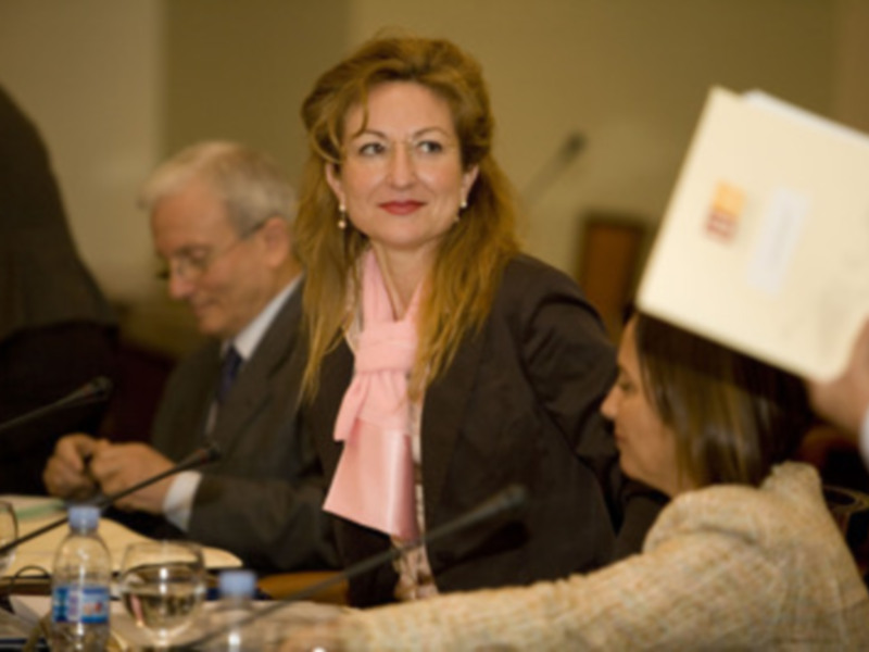 Mujer sonriente en una reunión de negocios, rodeada de documentos y micrófonos.