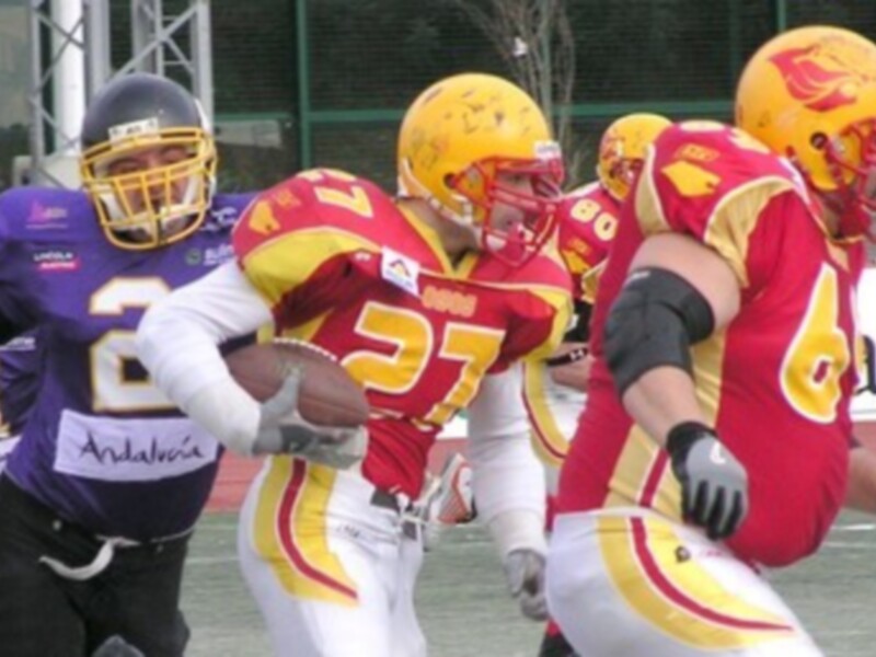 Jugadores de fútbol americano en acción durante un partido, con uniformes rojos y amarillos y cascos de color amarillo.