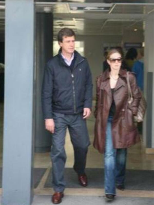 Una pareja camina juntos por un pasillo interior, ambos vestidos con abrigos de invierno y ropa casual, en un entorno urbano.