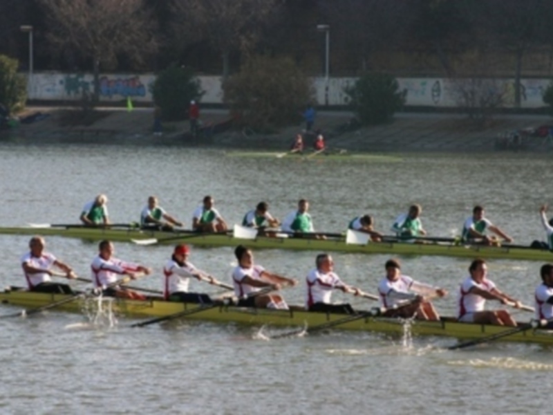 Equipo de remo en acción en un lago, con barcos y remos en el agua.