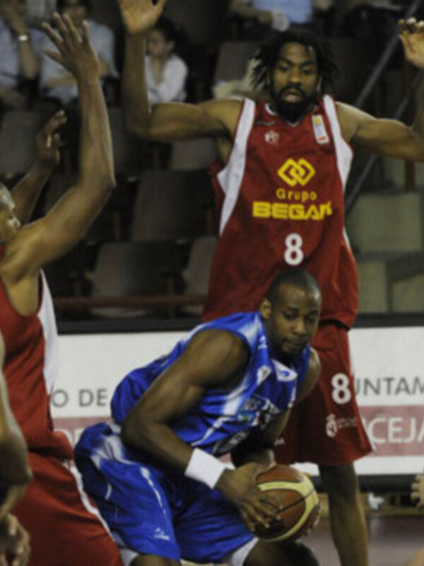Un jugador de baloncesto en acción, con el número 8 en su camiseta, mientras su equipo defiende en el fondo.