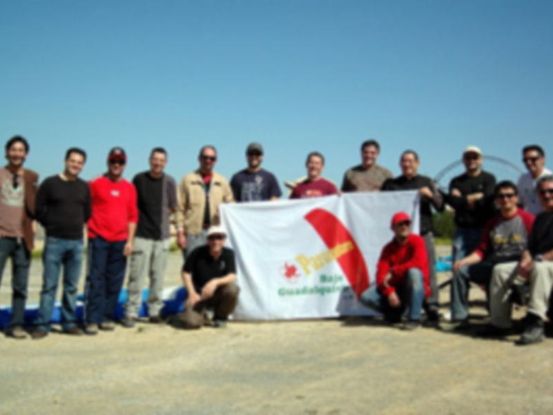 Equipo de motociclistas posando con su bandera en un día soleado al aire libre.