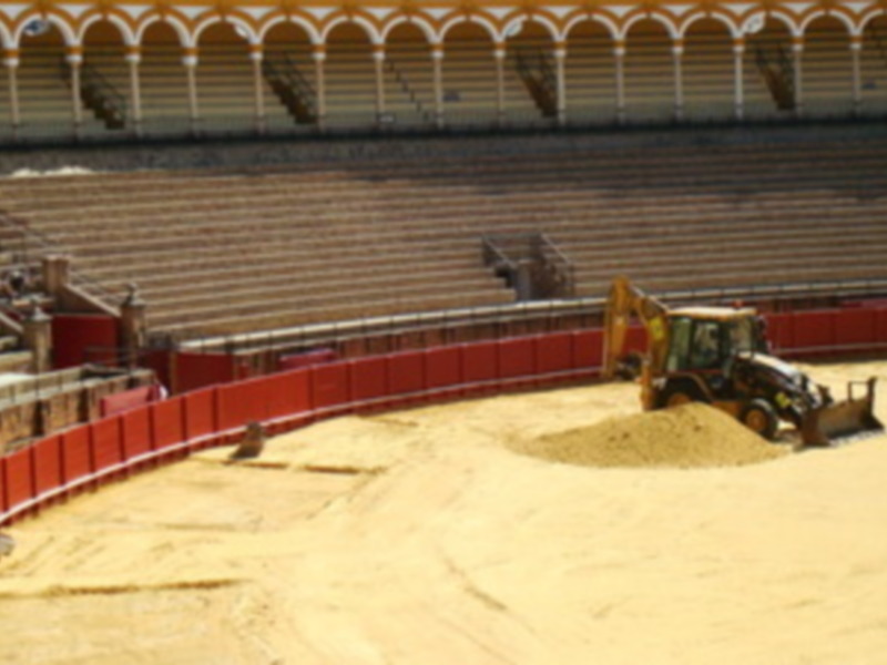 Obras de mantenimiento en una plaza de toros, con un tractor trabajando en el terreno.