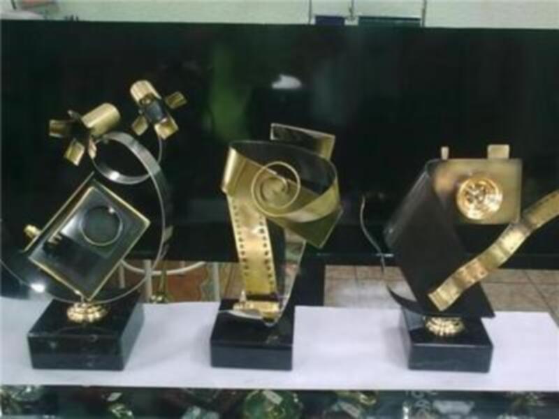Estatuetas de premios con bases de cristal y detalles dorados, posiblemente representando premios de cine, con un fondo de pantalla negro.