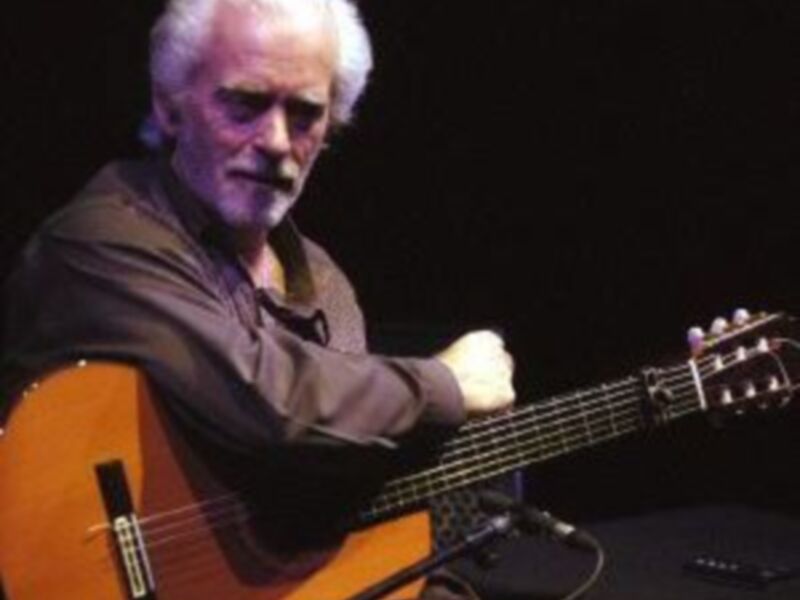 Un músico tocando una guitarra acústica en un escenario oscuro.