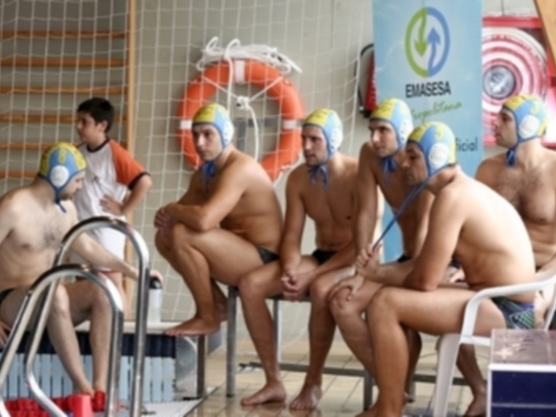 Equipo de waterpolo sentado en la banqueta de un estadio de piscina, listo para un partido.
