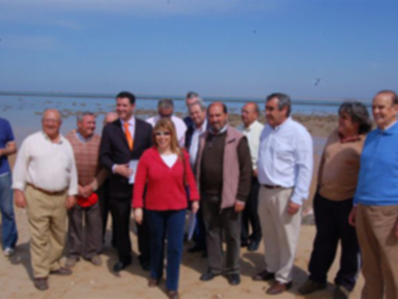Grup de persones posant per una fotografia en una platja. El cel és clar i hi ha una línia de mar al fons.
