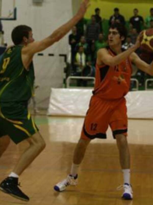 Jugadores de baloncesto en acción durante un partido, uno en verde y otro en naranja, en un entorno deportivo.