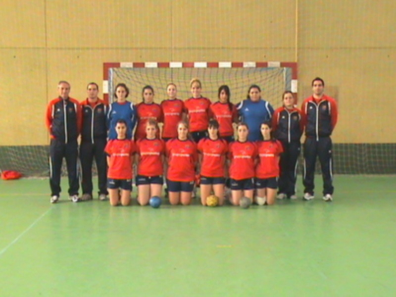 Equipo de balonmano femenino posando en un gimnasio con uniformes rojos y azules.