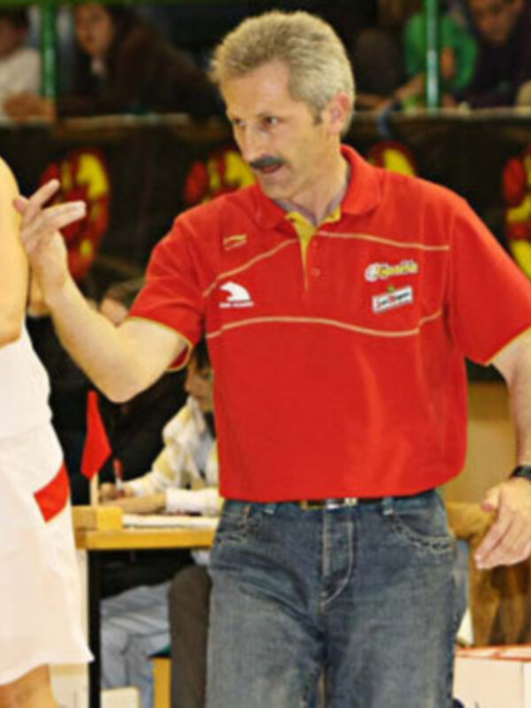 Entrenador en una cancha de baloncesto, interactuando con un jugador durante un juego.