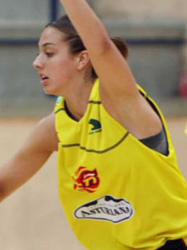 Jugadora de baloncesto en acción durante un entrenamiento, vestida con una camiseta amarilla y negra con el logo 'Asturiano'.