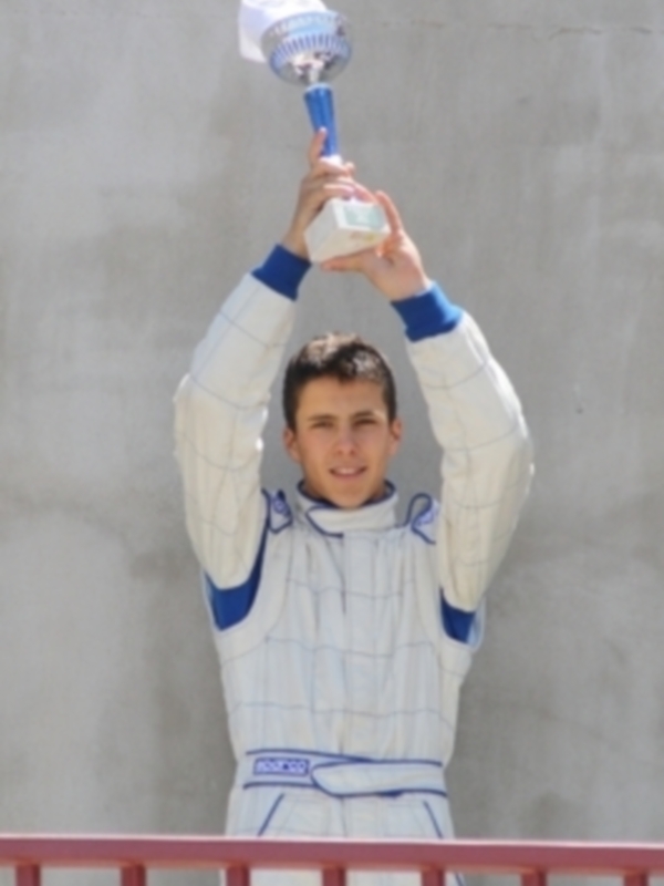 Joven piloto de karting celebrando con su casco y guantes en la mano.
