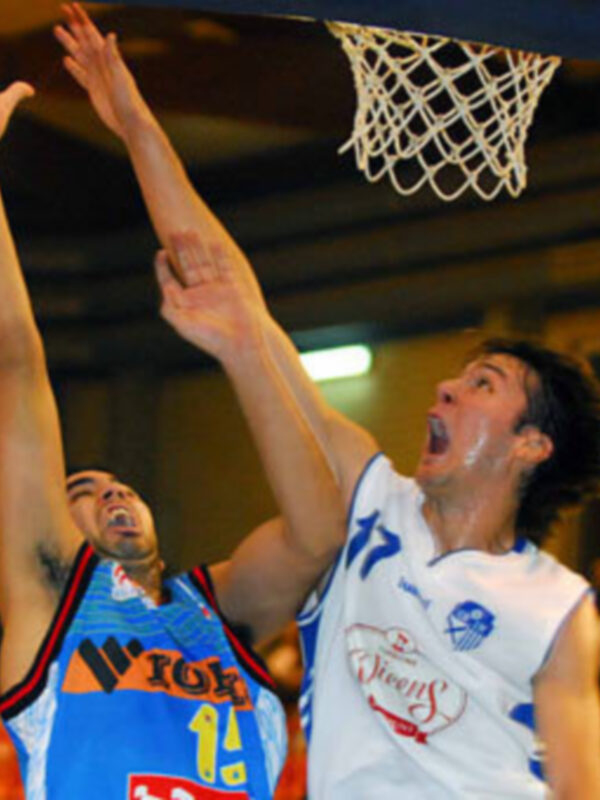Jugadores de baloncesto en acción durante un partido, uno intenta marcar mientras el otro bloquea.