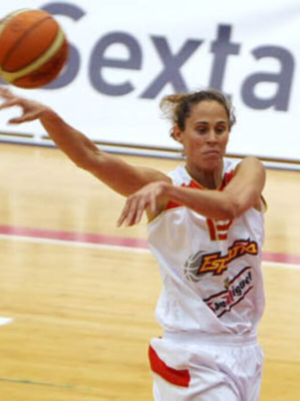 Una jugadora de baloncesto en acción, lanzando el balón en un partido de la Liga de Baloncesto Femenina. La imagen muestra a la jugadora con una camiseta blanca con detalles rojos y una bandera en el fondo.