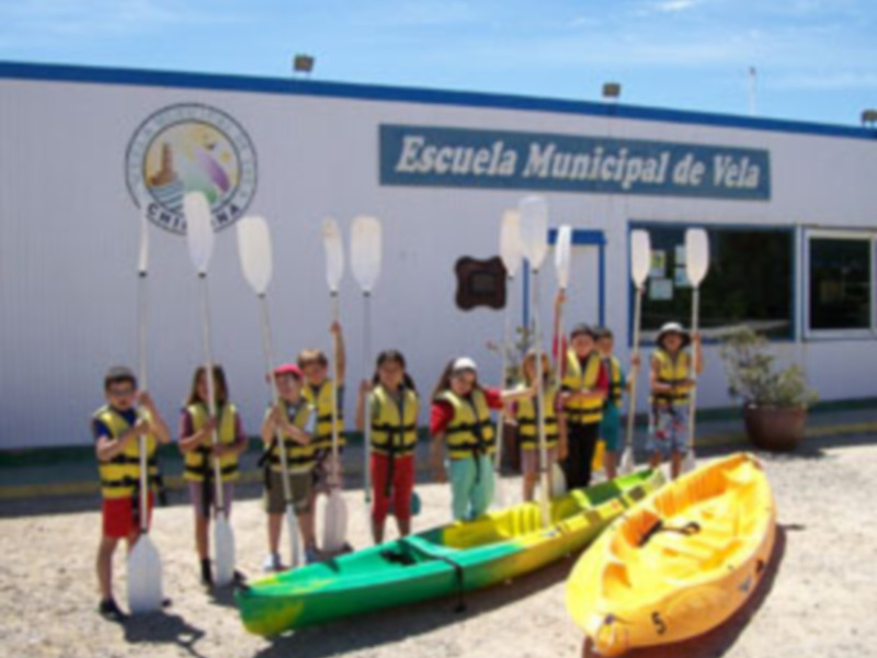 Estudiantes de la Escuela Municipal de Vela posan con sus kayaks y remos en un día soleado.
