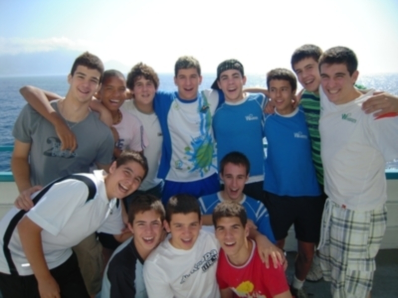Un grupo de amigos adolescentes posando juntos en la orilla del mar, sonriendo y divirtiéndose.