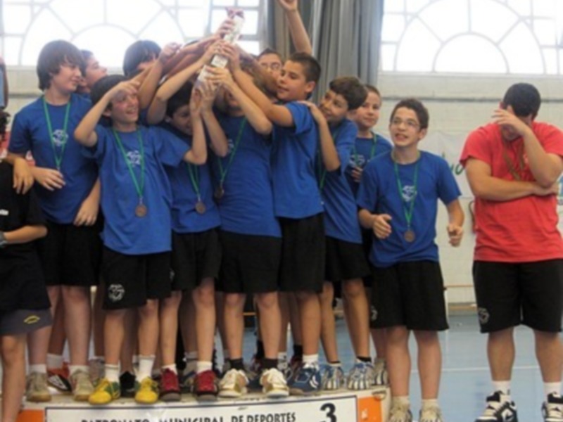 Equipo de baloncesto celebrando con el trofeo en el podio del torneo municipal de deportes.