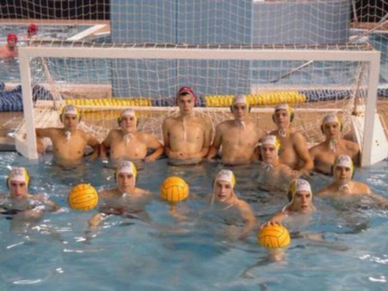 Equipo de waterpolo posando en la piscina con pelotas de waterpolo en la mano.