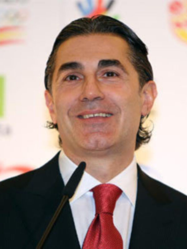 Persona en traje y corbata roja, fondo con logos de organizaciones.