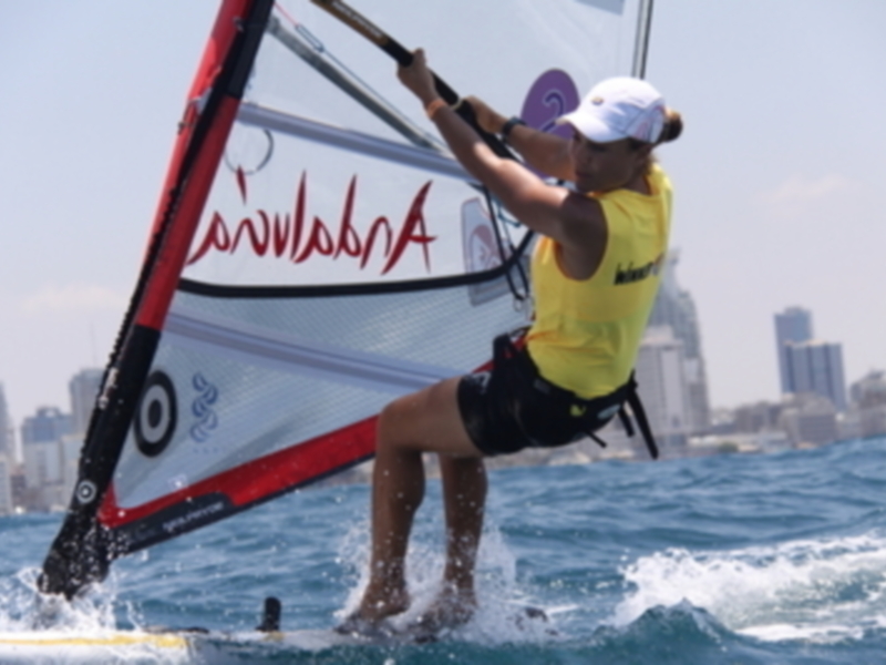 Un windsurfista en acción en un día soleado, navegando con destreza a lo largo de las olas frente a una ciudad costera.