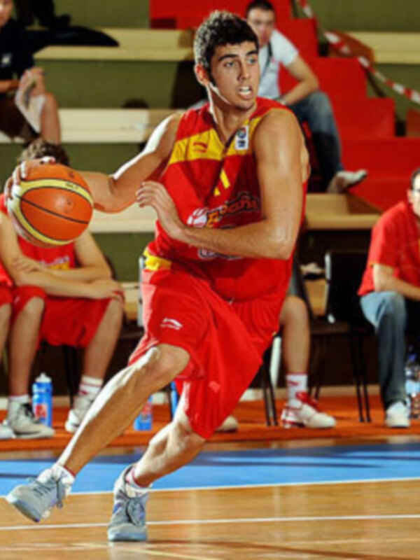 Jugador de baloncesto en acción con la pelota durante un partido. Uniforme rojo y blanco, entusiasta y concentrado.