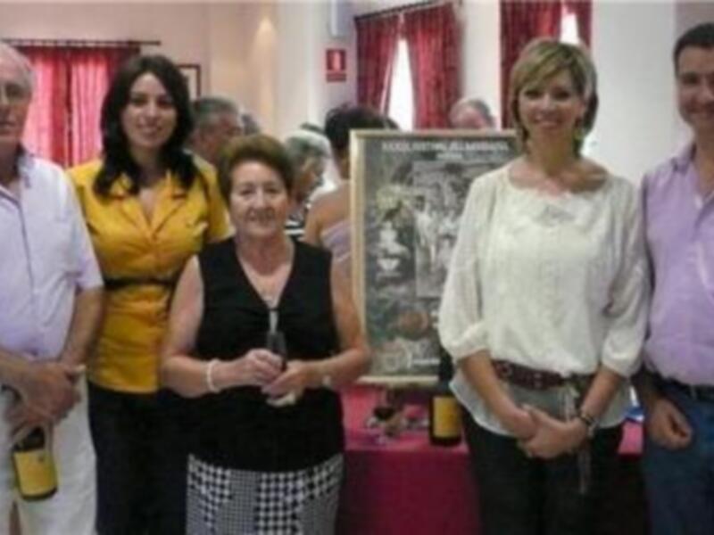 Una foto de grupo en un evento, con una mujer en el centro posando junto a otros participantes. En el fondo, se puede ver un cartel con información sobre el evento.