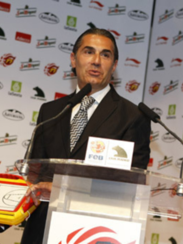 Un hombre en traje y corbata hablando en un podium con logos de empresas en el fondo.
