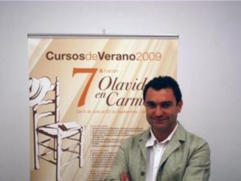 Persona posando frente a un cartel de los 'Cursos de Verano 2009' de la Universidad de Alcalá de Henares, España.