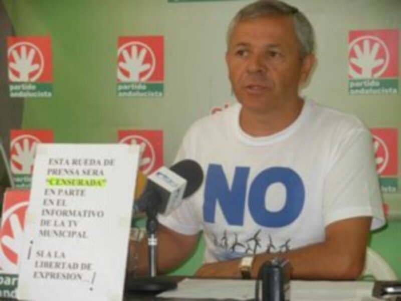 Un hombre habla en una conferencia de prensa, con un fondo de banderas rojas y blancas. La imagen muestra un microfono y un fondo con texto informativo sobre la libertad de expresión municipal.