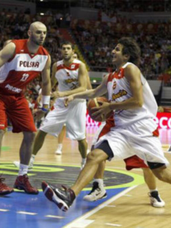 Jugadores de baloncesto en acción durante un partido en un estadio lleno de espectadores.