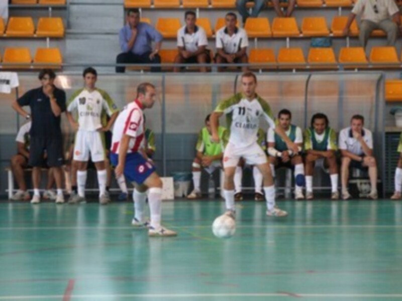 Jugadores de fútbol sala en acción durante un partido, con espectadores en el fondo.
