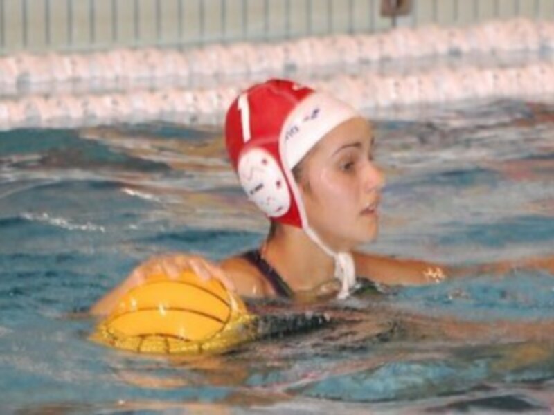 Joven jugando waterpolo en una piscina, sosteniendo un balón amarillo.
