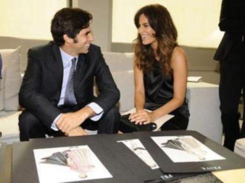 Dos personas sonrientes en una reunión profesional, rodeadas de diseños de moda en una mesa.