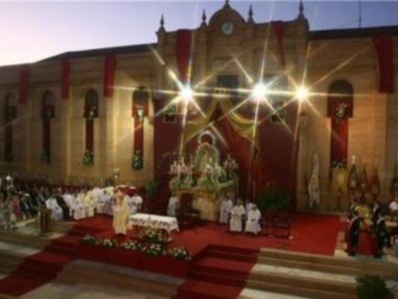 Eucaristía en una iglesia adornada con rojo y blanco, con sacerdotes y fieles participando en la ceremonia.