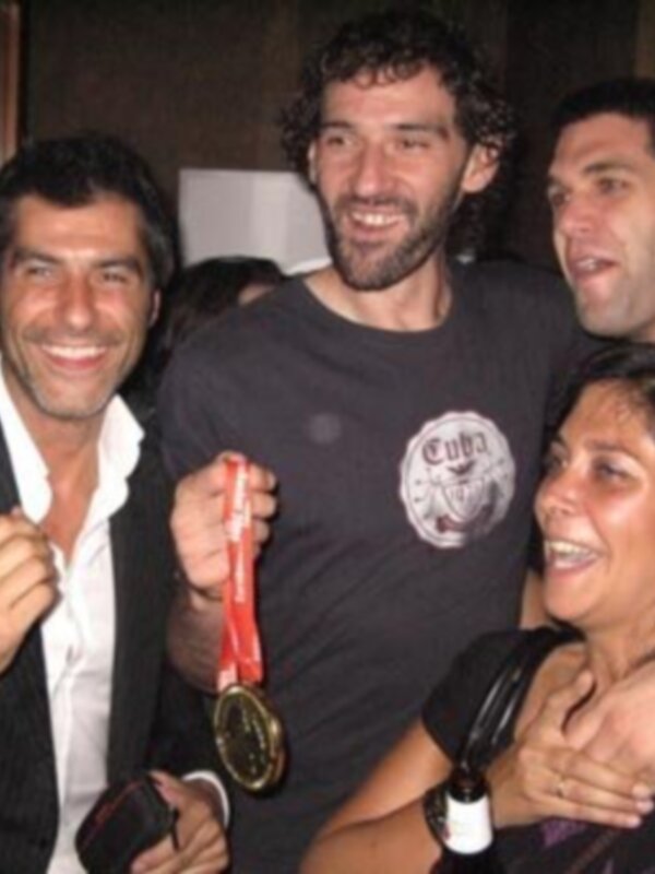 Tres personas sonrientes, una de ellas sostiene una medalla roja.