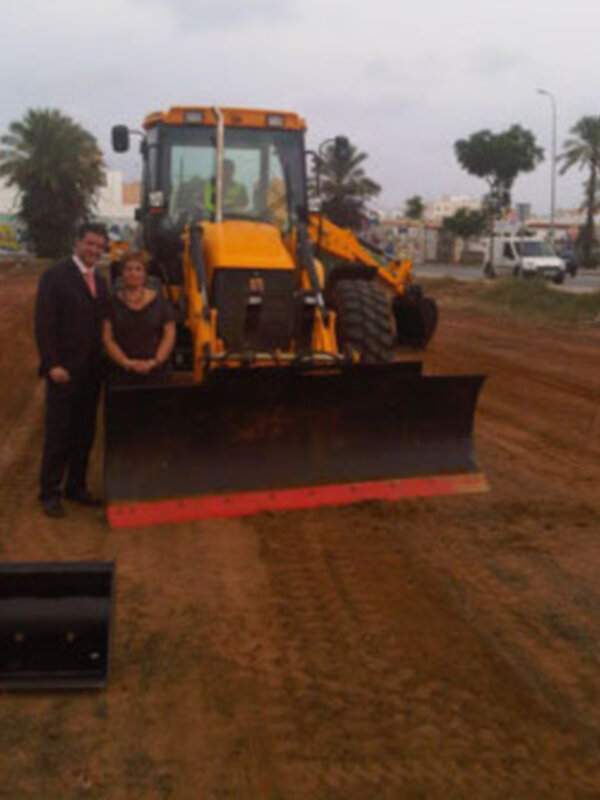 Dos personas posan junto a un tractor en una obra de construcción.