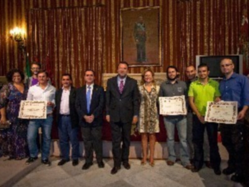 Celebración de premios en un salón decorado con dorado, con personas sosteniendo certificados.