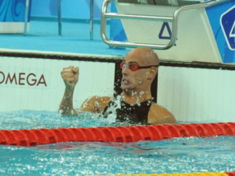 Atleta nadando con fuerza en una piscina olímpica, con el brazo levantado en señal de victoria.
