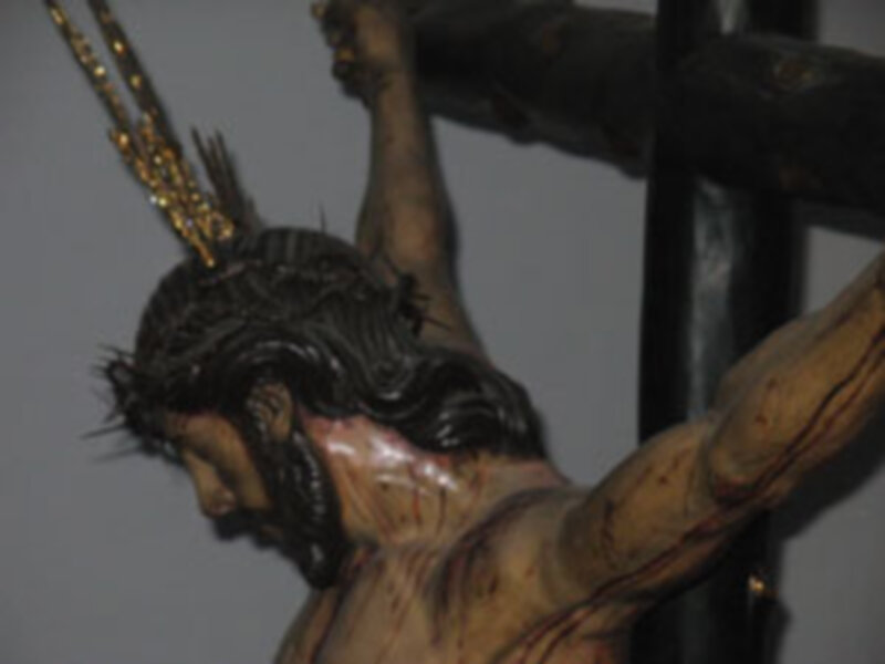 Detalle de una escultura religiosa que muestra a un personaje con una corona de espinas en la cabeza, sosteniendo una cruz.