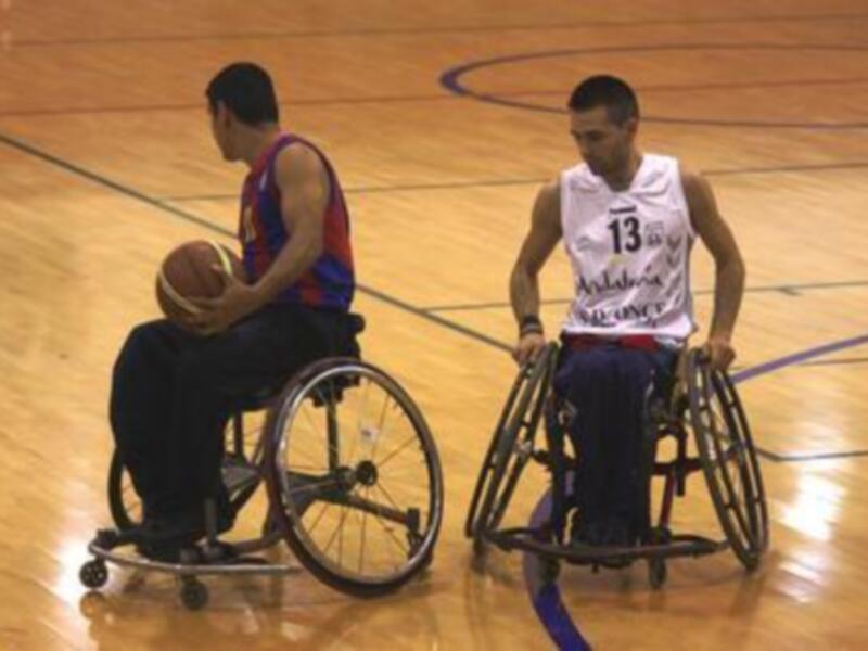 Jugadores de baloncesto en silla de ruedas en un partido en una cancha deportiva.