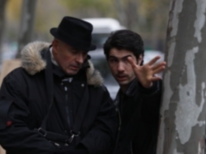 Dos hombres conversando en la calle, uno de ellos señala hacia el cielo.