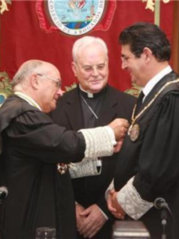 Entrega de medalla en una ceremonia formal con vestimenta oficial y presencia de un sacerdote