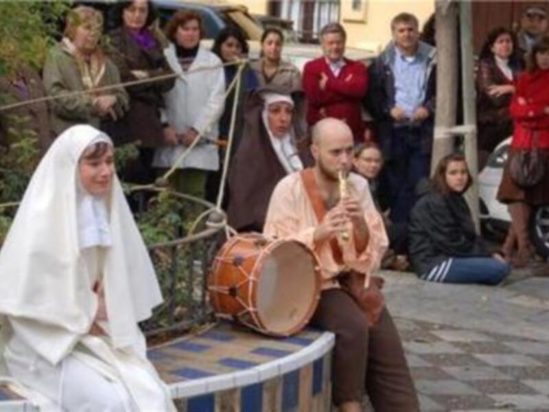 Un músico callejero toca el tambor y el clarinete mientras una monja pasa por él, con una multitud de espectadores observando la escena.