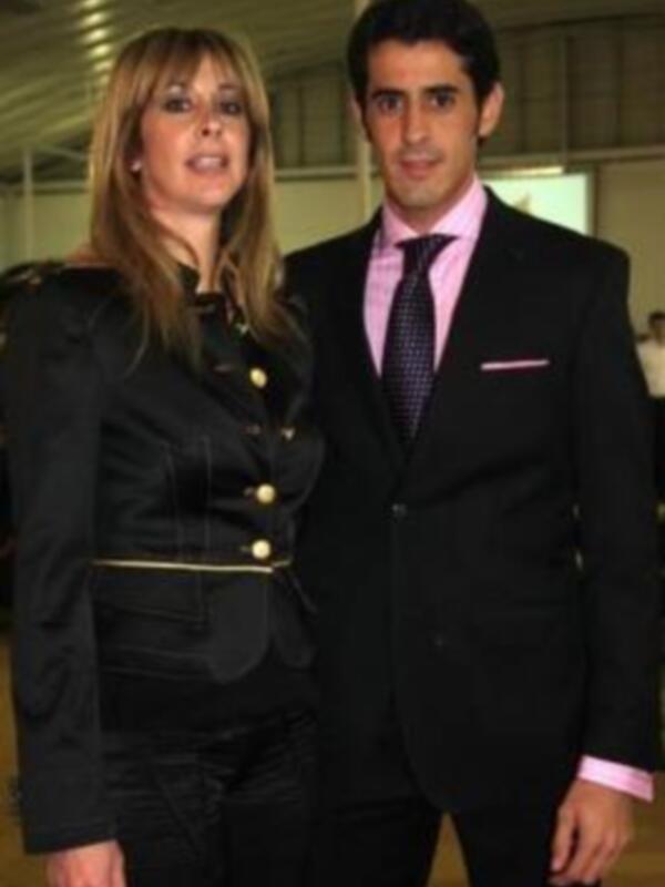 Dos personas posando juntos, una con traje militar y la otra con traje formal, en un entorno interior con iluminación artificial.