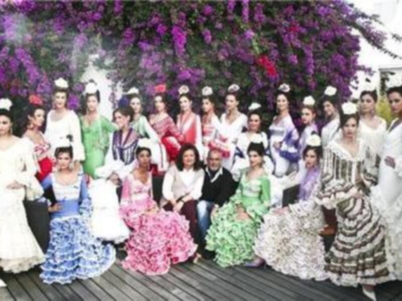 Desfile de trajes de flamenca con modelos posando al aire libre en un entorno floral.