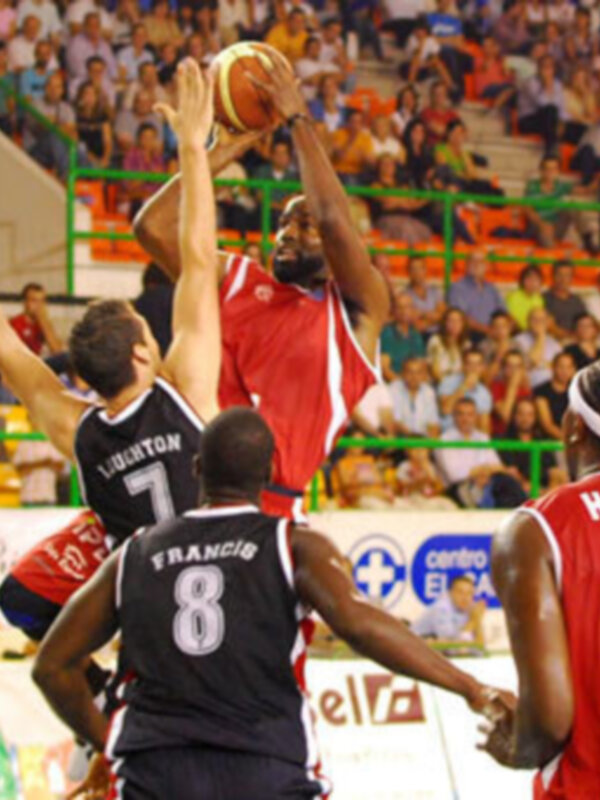 Un partido de baloncesto en un estadio lleno de espectadores. Los jugadores están en acción, con un balón en el aire.